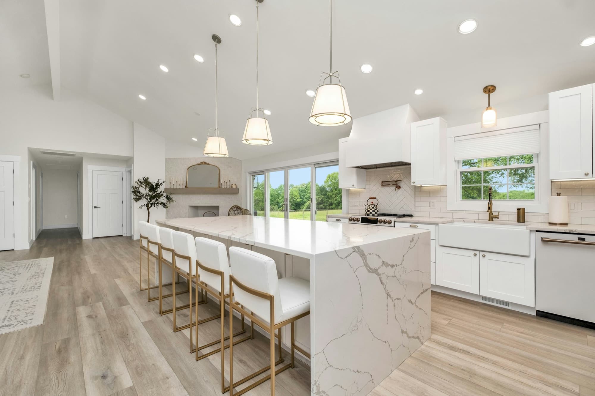 A bright, spotless kitchen with a white marble island, gold bar stools and garden views